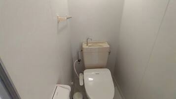 Un baño pequeño y blanco con un inodoro, un bidé y un cubo de basura.