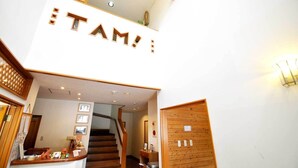 A hotel entrance with a staircase, wooden decor, and a sign reading 'TAM!'