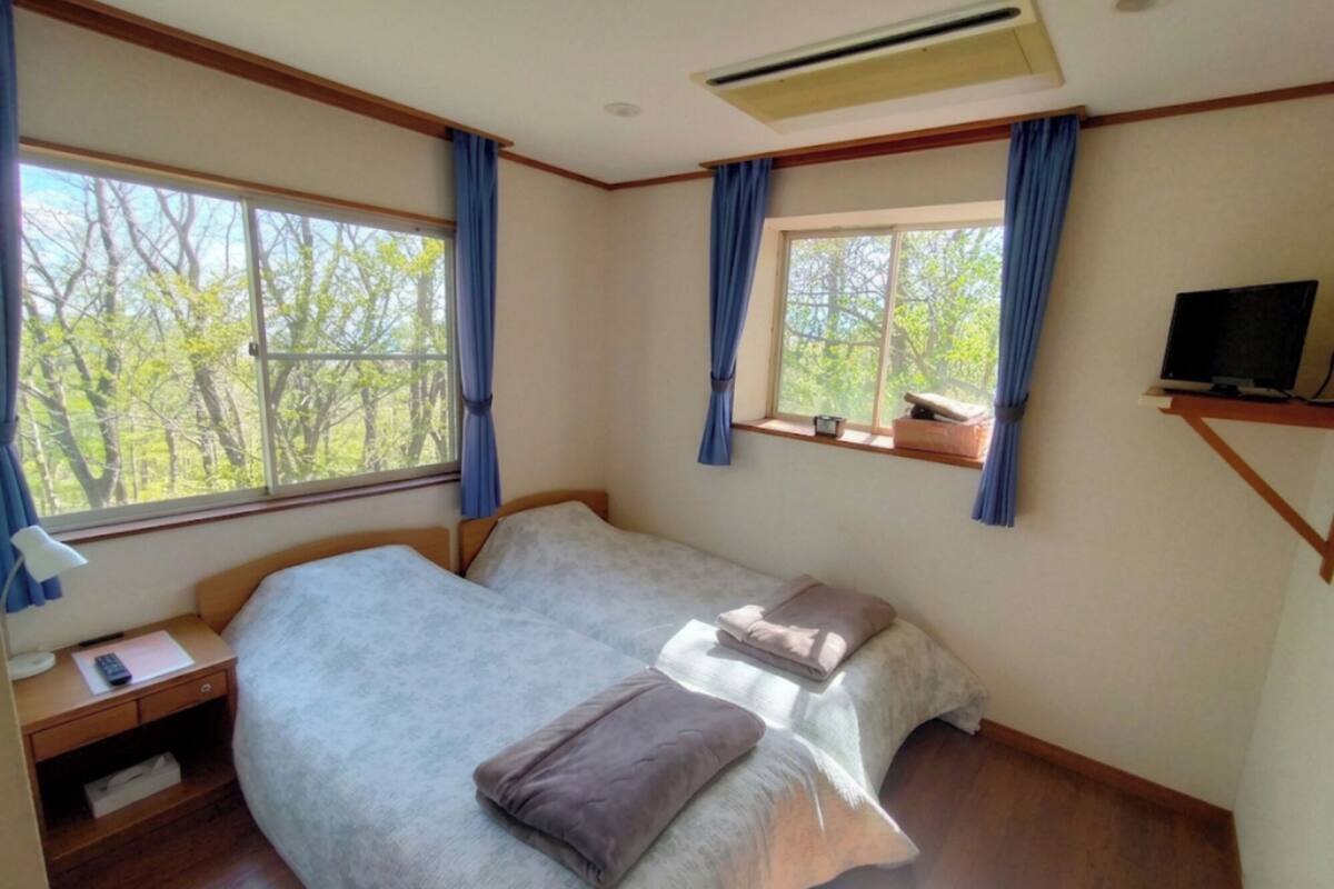A bedroom with a bed, a desk, a TV, and a window with curtains.