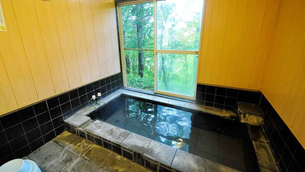 A bathroom with a bathtub, a window, and a wooden wall.