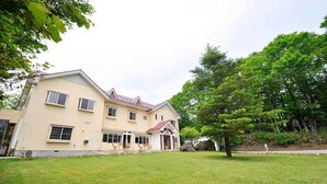 A two-story building with a red roof, a covered patio with outdoor furniture, and a well-maintained lawn.