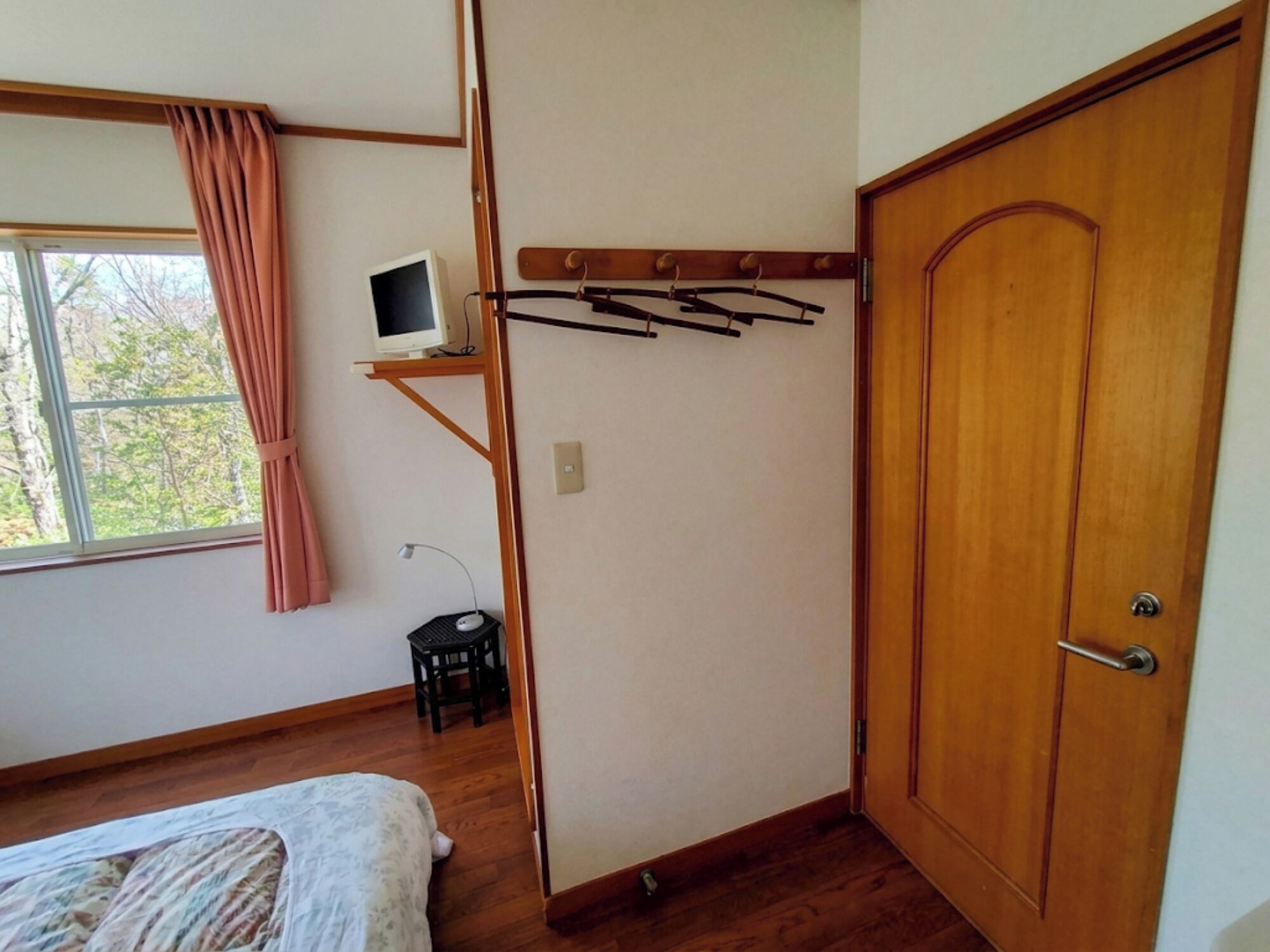 A room with a bed, a desk with a computer, a wooden door, and a window with curtains.