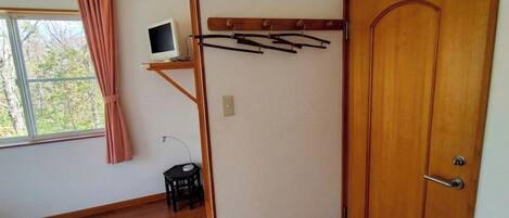 A room with a bed, a desk with a computer, a wooden door, and a window with curtains.