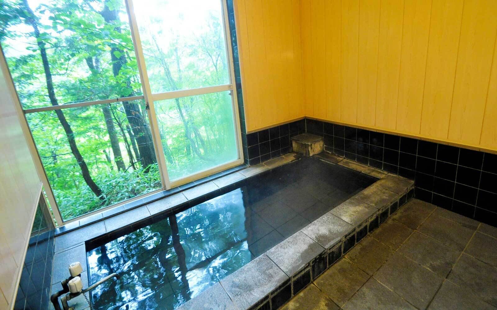 A hot tub with a view of a forest through a large window.