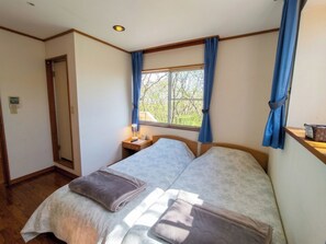 A room with a bed, a bedside table, a window with curtains, and a door. - Pention TAM (Nasu)
