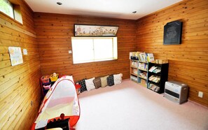 A room with wooden walls, a window, a bookshelf, a crib, and a heater. - Pention TAM (Nasu)