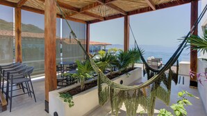 A covered outdoor area with a hammock, tables, chairs, and potted plants. - Chic Nomada Loft with Infinity Pool Romantic Zone (Puerto Vallarta)