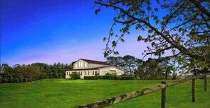 A large, two-story house with a red roof, surrounded by a well-maintained lawn and trees. - Peninsula Farm heated spa, fireplace & fire pit (Somerville)