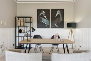 A modern room with a wooden table, black chairs, a black lamp, a black bookshelf, and two wall-mounted paintings of birds. - Peninsula Farm heated spa, fireplace & fire pit (Somerville)