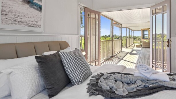 A bedroom with a bed, pillows, a blanket, and a view of an outdoor deck and garden. - Peninsula Farm heated spa, fireplace & fire pit (Somerville)