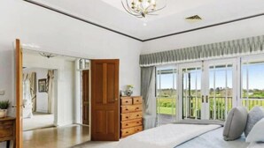 A bedroom with a large bed, a wooden dresser, a door leading to a balcony, and a view of the outdoors. - Peninsula Farm heated spa, fireplace & fire pit (Somerville)