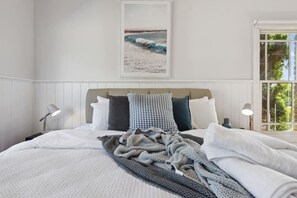 Un lit bien fait, recouvert d’une couverture à motifs, une tête de lit agrémentée de plusieurs coussins, des lampes de chevet et un tableau encadré accroché au mur.