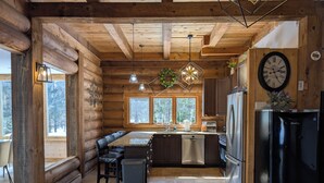 Cucina in stile baita con isola centrale, travi in legno, frigorifero in acciaio inossidabile e un orologio appeso al muro.