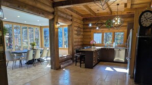 Interno di una baita in legno con zona pranzo, cucina e ampie finestre.