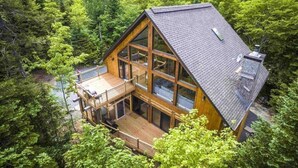 Una baita con veranda, ampie finestre e tetto spiovente, immersa in una fitta foresta.