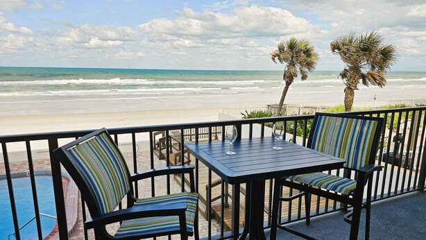 Un balcon avec une table et des chaises donnant sur une plage et une piscine.