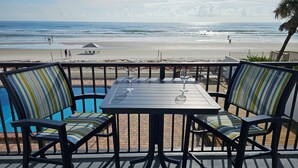 Une terrasse au bord de la plage, avec une table et des chaises, d’où l’on a une vue sur l’océan.