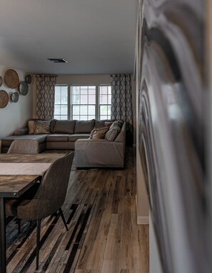 A modern living room with a sectional sofa, a dining table with chairs, and a patterned wall.