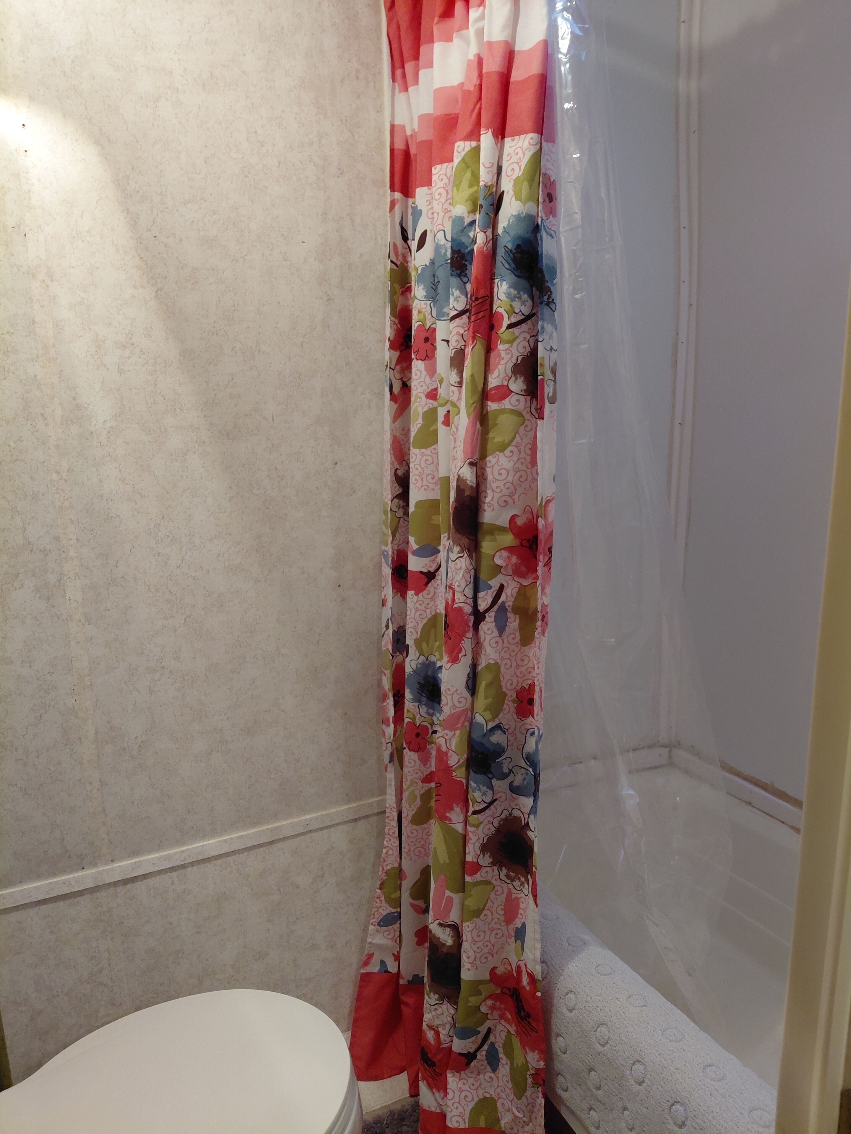 Ein Badezimmer mit Toilette, einer Duschkabine mit Blumenmuster und einer weißen Badewanne.