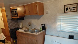 Une cuisine compacte avec des meubles de rangement en bois, un four à micro-ondes, une cuisinière et une machine à café.