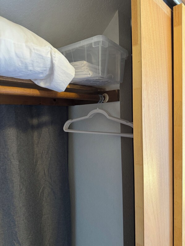 A closet with a wooden shelf, plastic storage bins, and a white hanger.