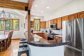 Eine moderne Küche mit Holzschränken, einem Edelstahlkühlschrank und einer großen Kochinsel mit Sitzgelegenheiten.
