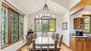 A dining room with a large wooden table and chairs, a chandelier, and large windows with a view of trees. - Family Friendly Retreat W/Hot Tub-- 8 min to Vail (Vail)