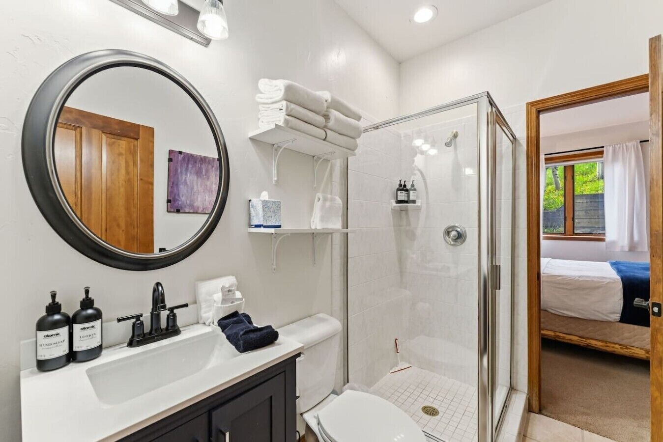 A modern bathroom with a round mirror, white sink, and a glass-enclosed shower.