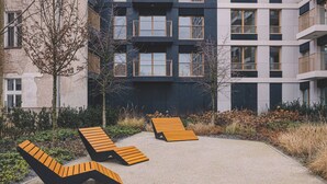 A modern building with multiple balconies, a paved outdoor area with lounge chairs, and a garden with shrubs and trees. - Central Bydgoszcz Getaway Close to Attractions (Bydgoszcz)