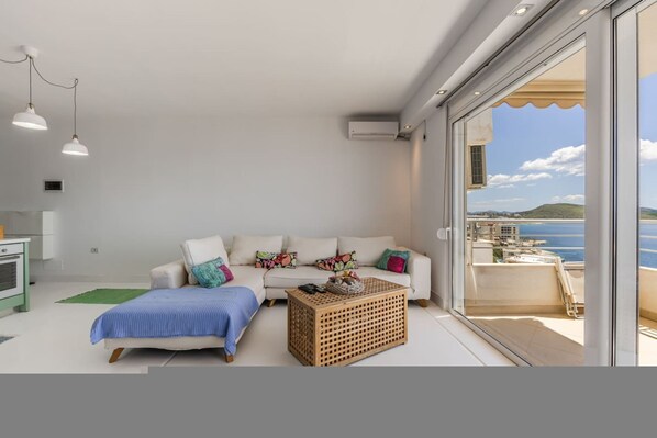 A modern living room with a sofa, a coffee table, and a view of the sea. - Sunkissed Apartment 1BR Amazing Views by the Sea (Sarandë)