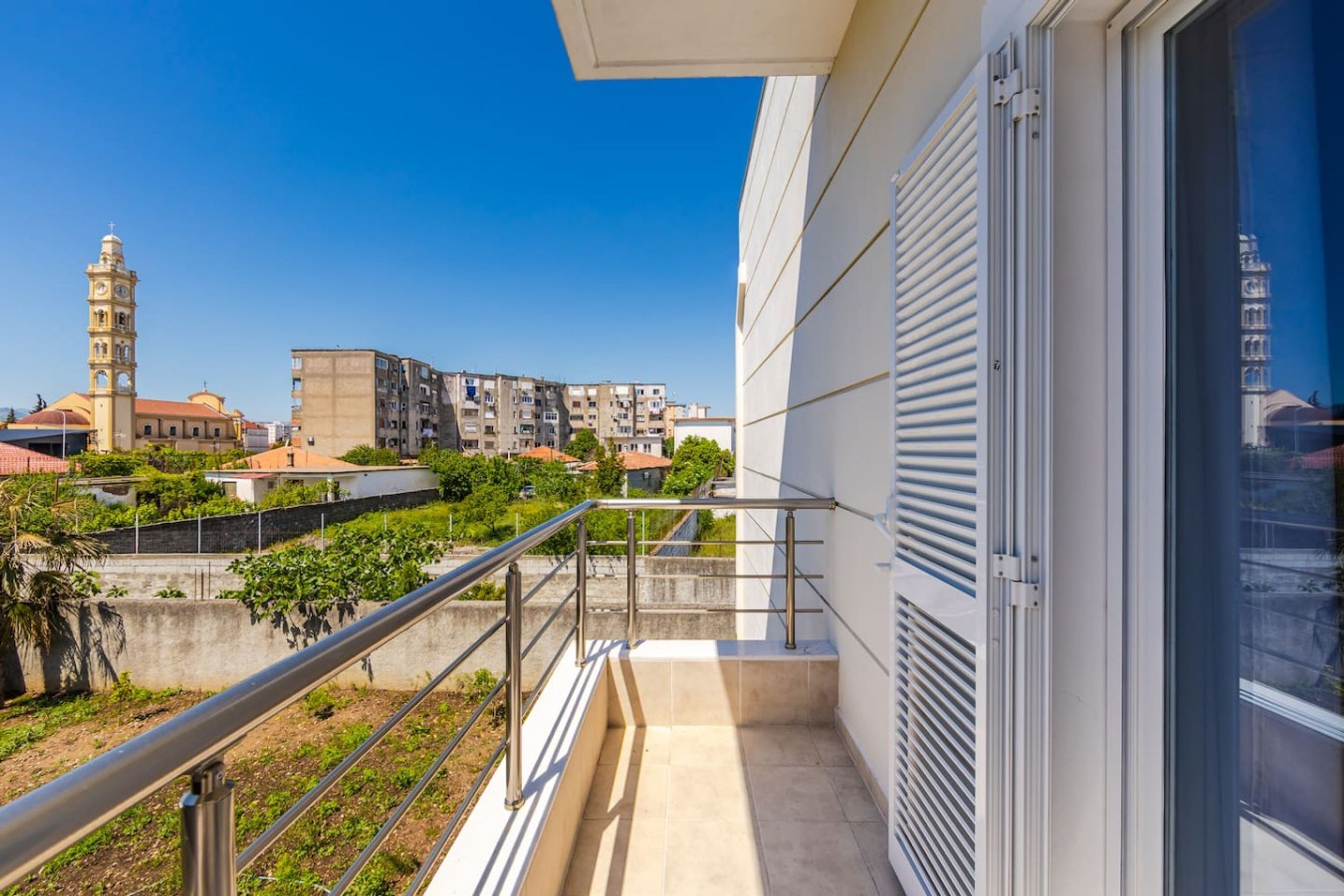 A balcony with a metal railing, a view of a mosque with a minaret, and residential buildings in the background.