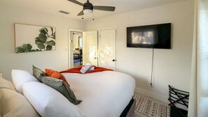 A bedroom with a bed, a ceiling fan, a TV, and a door leading to another room. - Modern Miami Retreat w/ Games (Miami)