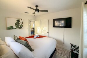 Ein Schlafzimmer mit Bett, Deckenventilator, Fernseher und einer Tür zu einem anderen Raum.