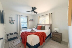 A bedroom with a bed, bedside table, nightstand, wall-mounted TV, ceiling fan, window with blinds, and a wall-mounted light fixture. - Modern Miami Retreat w/ Games (Miami)