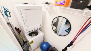 A compact laundry area with a washing machine, a small exercise ball, and a mirror. - Modern Miami Retreat w/ Games (Miami)