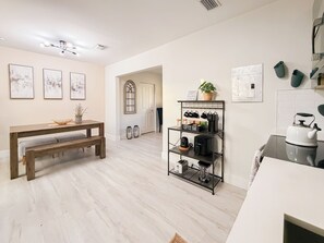 A modern kitchen with a coffee bar, a dining area with a bench, and a hallway with a door. - Modern Miami Retreat w/ Games (Miami)