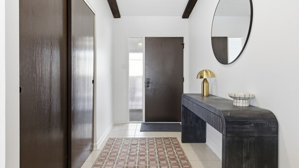 A hallway with a dark wooden door, a glass door, a black console table with a gold lamp, and a white wall with a round mirror. - Gorgeous 3-bedroom house with AC in pleasant Fishers (Fishers)