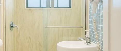 A bathroom with a shower, toilet, and sink, featuring a wooden door and tiled walls.