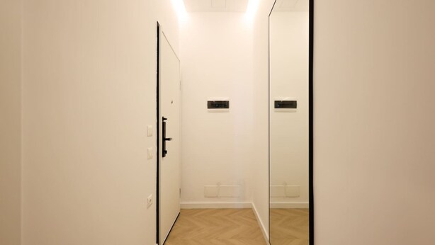 Un pasillo estrecho con suelo de madera, una puerta a la izquierda y un espejo grande a la derecha.