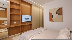 Una camera d'hotel moderna con televisione integrata, scaffali in legno, un letto e un quadro appeso al muro.