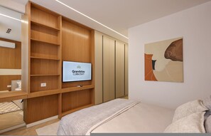 A modern hotel room with a built-in TV, wooden shelving, a bed, and a painting on the wall. - Grandstay Sea Penthouse 02 (Durrës)