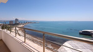 A balcony with a view of the sea, a beach, and a modern building. - Grandstay Sea Penthouse 01 (Durrës)
