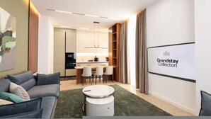 A modern living room with a sofa, a round coffee table, and a kitchen in the background. - Grandstay Sea Penthouse 01 (Durrës)