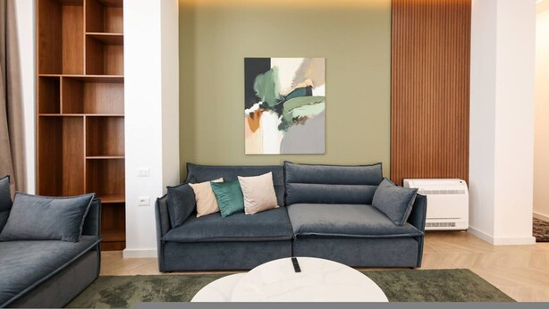 A modern living room with a grey sofa, a white coffee table, and a wooden shelving unit. - Grandstay Sea Penthouse 01 (Durrës)