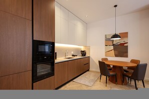 A modern kitchen with wooden cabinets, a built-in oven, a dining table with chairs, and a pendant light. - Grandstay Sea Penthouse 04 (Durrës)