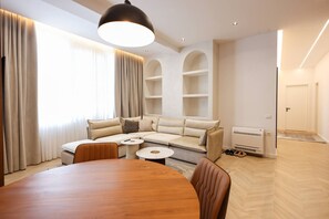 A modern living room with a large wooden table, a beige sofa, and a built-in shelving unit. - Grandstay Sea Penthouse 04 (Durrës)