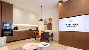 Une cuisine moderne avec un coin repas, un grand écran diffusant la collection « Grandstay », et un espace salon confortable.