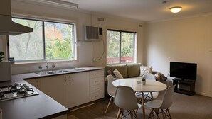 Cucina compatta con angolo ristoro, TV e finestra vista alberi.