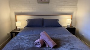 Un letto rifatto con cura, un asciugamano arrotolato, due lampade da comodino e un quadro appeso al muro.