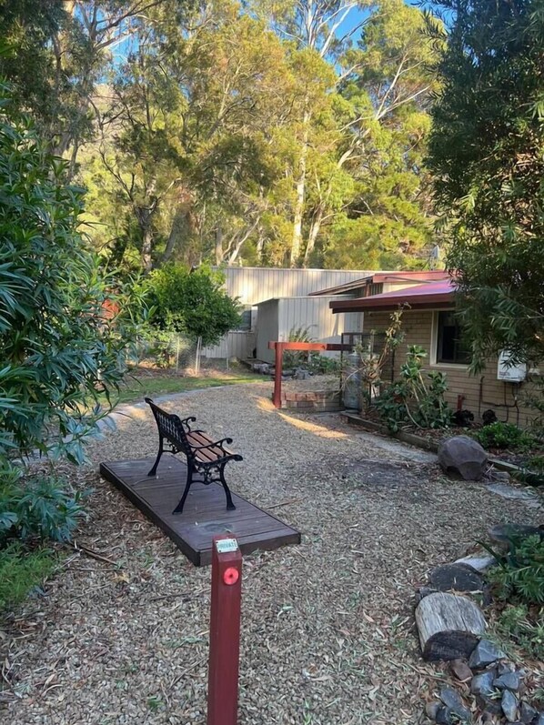 A garden with a bench, a wooden deck, and a building with a red roof.